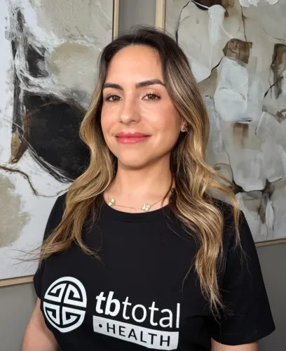 Woman wearing TBTotal Health shirt smiling indoors – telemedicine wellness brand team member