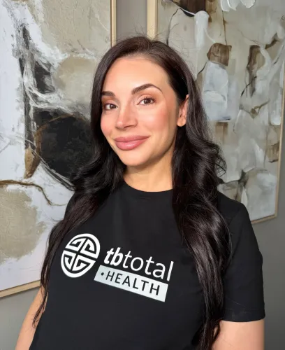“Woman wearing TBTotal Health shirt smiling indoors – telemedicine wellness brand representative